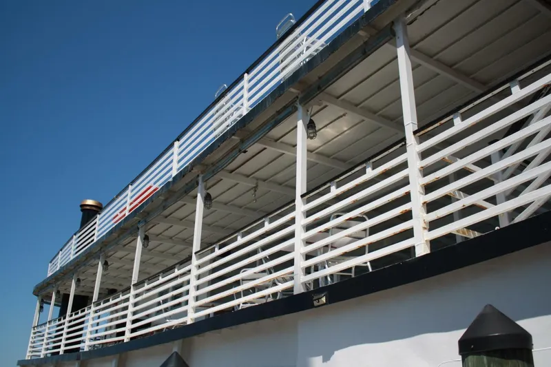 Slide: The Image of A two-story paddle wheel boat with white railings and a black smokestack under clear skies. - 15