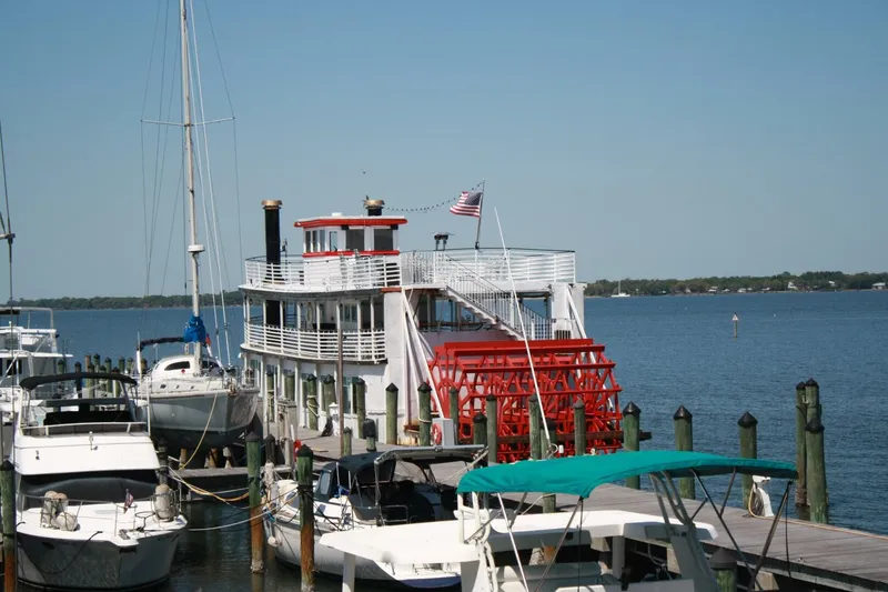 Slide: The Image of A white paddle wheel boat with a red wheel docked, surrounded by sailboats. - 11
