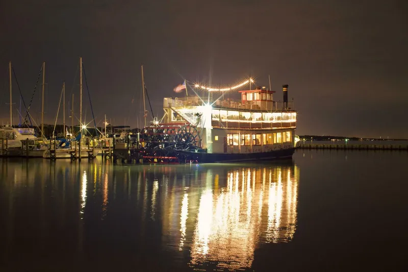 Slide: The Image of A lit paddle wheel boat is docked at night, surrounded by sailboats. - 2