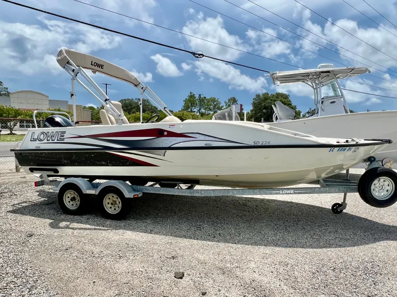 Slide: The Image of A white 2016 Lowe Sport Deck 224 boat on a trailer in a gravel lot. - 2