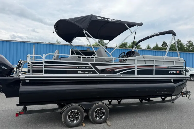 The Image of 2021 Ranger Reata 223FC pontoon boat on trailer, black with canopy, parked outdoors. - 0