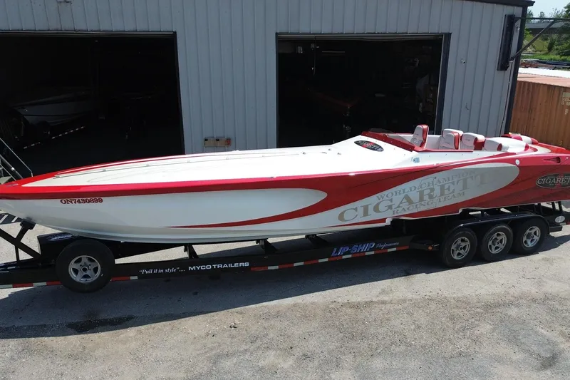 The Image of 2003 Cigarette 36' Gladiator speedboat on trailer, red and white design, parked outside a garage. - 1
