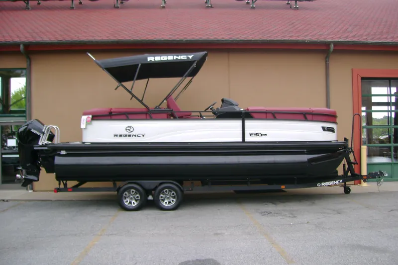 The Image of 2026 Regency 230 DL pontoon boat on trailer, parked outside a building. - 0