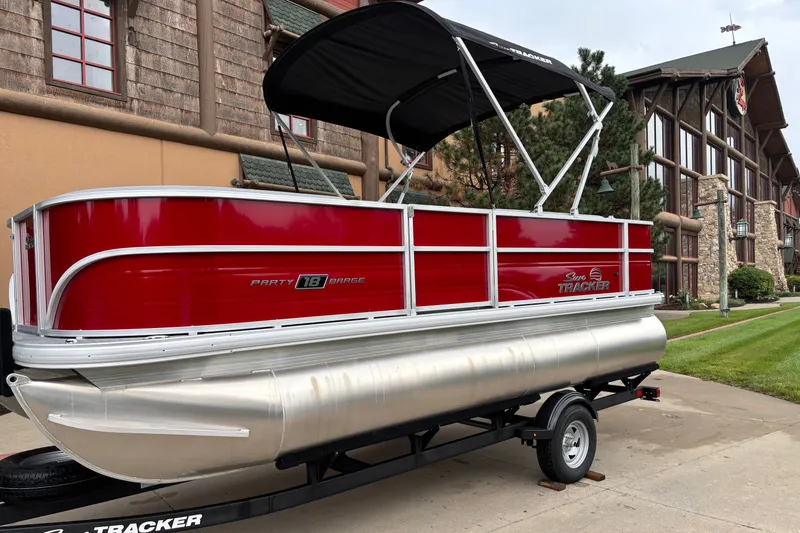 Slide: The Image of 2026 Sun Tracker Party Barge 18 DLX pontoon boat with red exterior, parked on a trailer. - 3