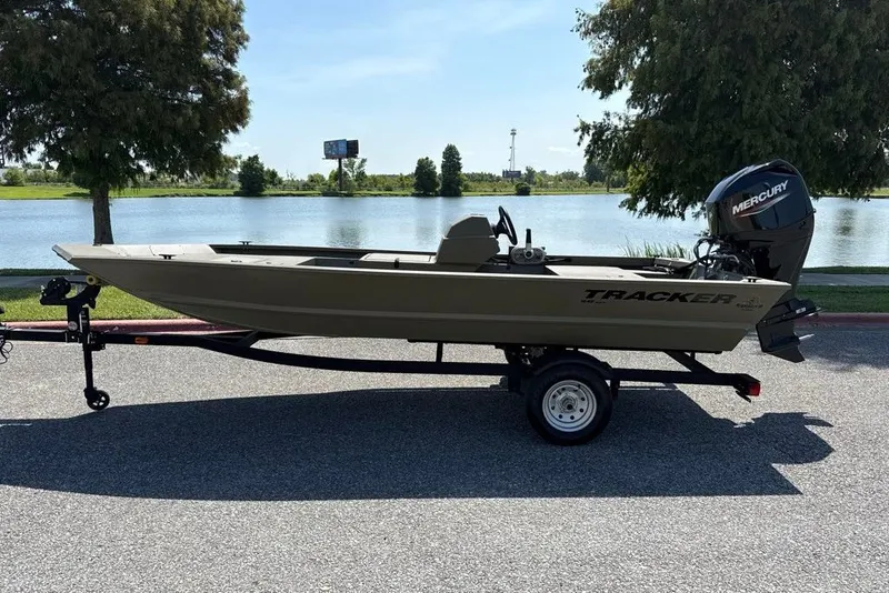 The Image of 2026 Tracker Grizzly 1648 SC boat on trailer by a lake, featuring Mercury outboard motor. - 0