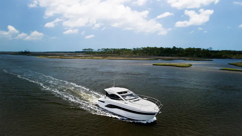 Slide: The Image of 2022 Bavaria SR41 yacht cruising on a serene river under a partly cloudy sky. - 2