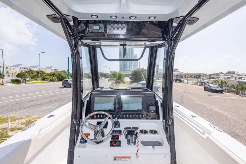 Slide: The Image of 2022 Sea Hunt Gamefish 27 helm with dual displays and steering wheel, docked near a road. - 19