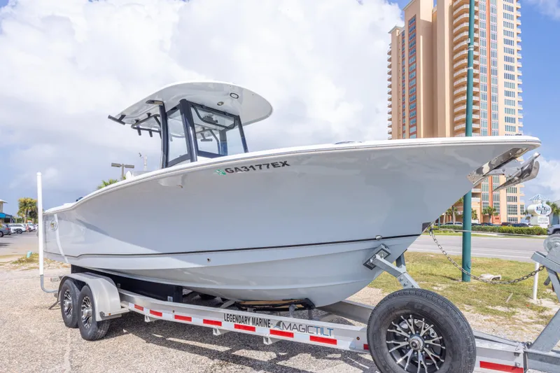 Slide: The Image of 2022 Sea Hunt Gamefish 27 boat on trailer, parked near tall building under cloudy sky. - 50
