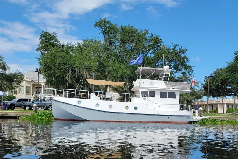 The Image of A 2007 Great Harbour N47 is docked by the water, surrounded by trees and buildings. - 0