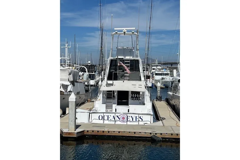 Slide: The Image of A 1994 Mikelson 64 yacht named "Ocean Eyes" docked at a marina under a clear sky. - 30