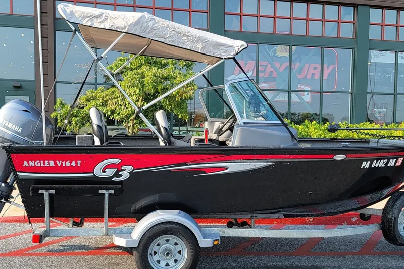 The Image of 2014 G3 Angler V164 F boat with canopy on trailer, parked outside a store. - 1