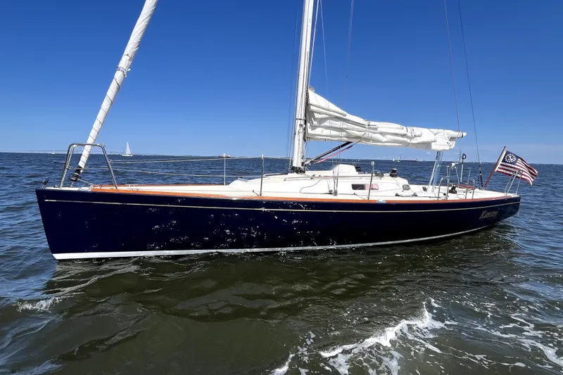 The Image of A 2006 J/100 sailboat glides on calm waters under a clear blue sky. - 0