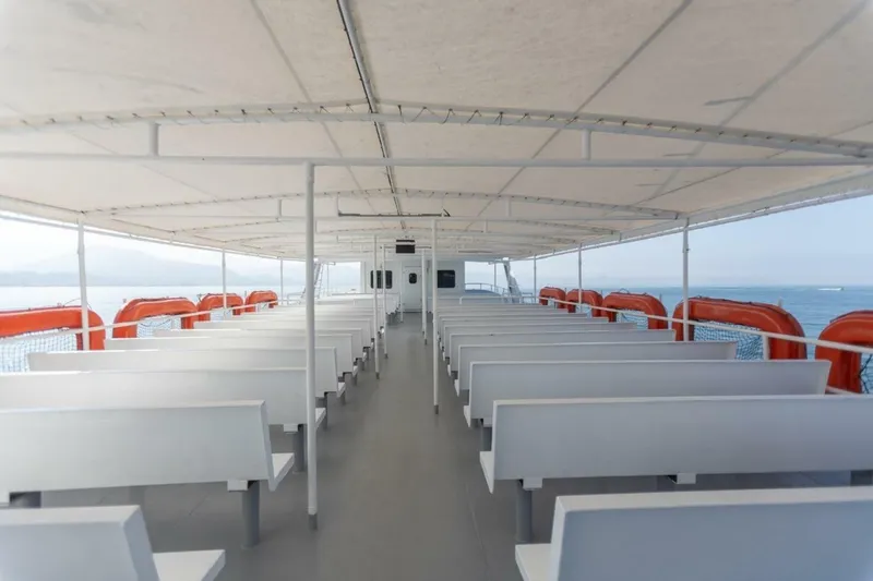 Slide: The Image of A spacious passenger deck with white benches and orange life rings on the sides. - 8