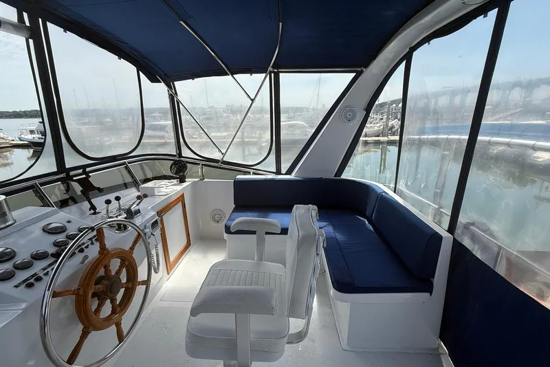Slide: The Image of 1985 DeFever 40 Offshore Cruiser helm with wooden wheel, blue seating, and marina view. - 15