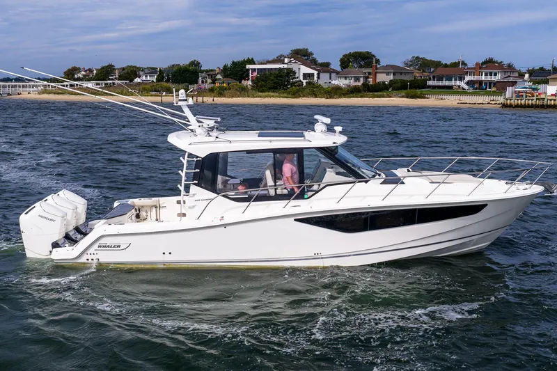 Slide: The Image of 2024 Boston Whaler 405 Conquest cruising on water near coastal homes. - 1