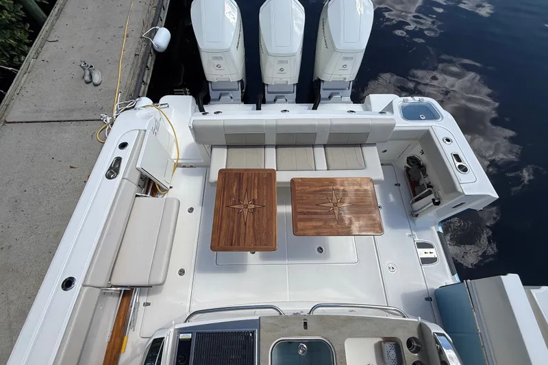 Slide: The Image of 2024 Boston Whaler 420 Outrage boat deck with seating and twin wooden tables. - 7