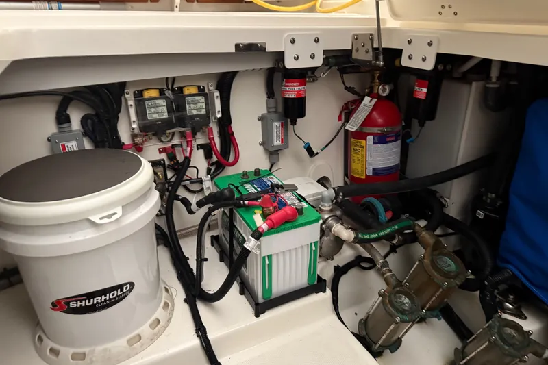 Slide: The Image of 2024 Boston Whaler 420 Outrage engine compartment with battery, fire extinguisher, and wiring. - 58