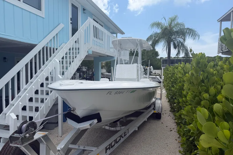 Slide: The Image of 2024 Contender 25 Bay boat on trailer beside a blue house and lush greenery. - 28