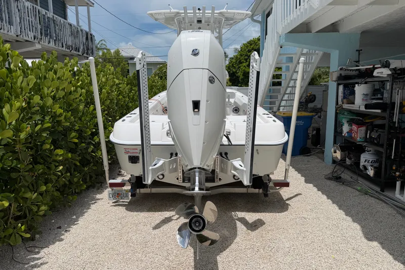Slide: The Image of 2024 Contender 25 Bay boat with outboard motor, parked on gravel near greenery. - 35