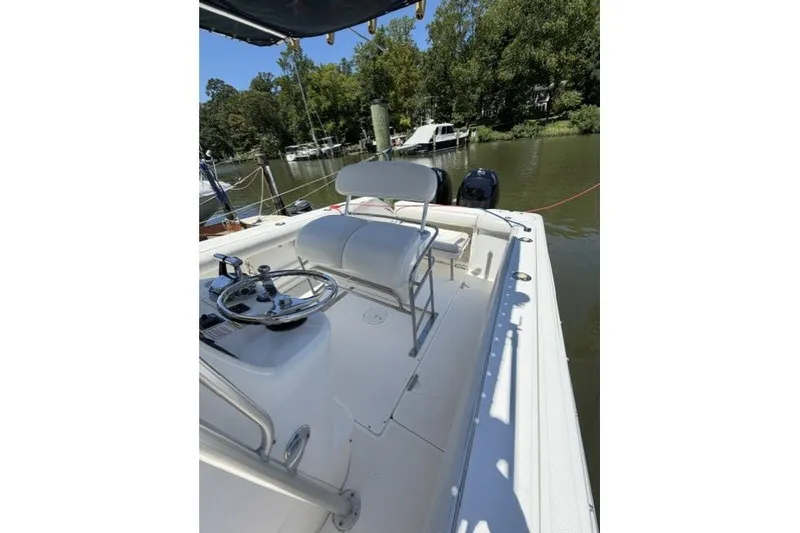 Slide: The Image of 2004 Boston Whaler 270 Outrage boat interior with steering wheel and seating, docked by a river. - 8
