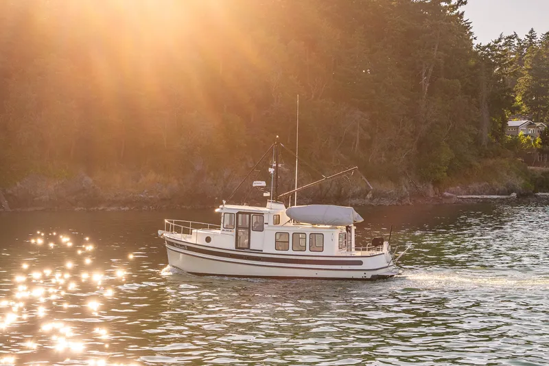 Slide: The Image of Nordic Tug 32 (2000) cruising on sunlit water near a forested shoreline. - 10