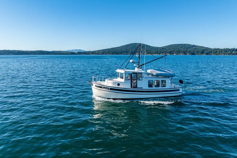 Slide: The Image of 2000 Nordic Tug 32 cruising on a serene lake with forested hills in the background. - 8