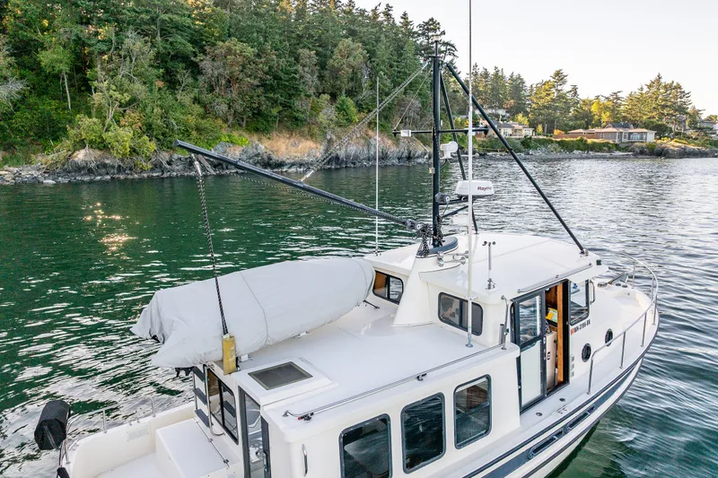 Slide: The Image of Nordic Tug 32 (2000) cruising near a forested shoreline, showcasing its classic design. - 18