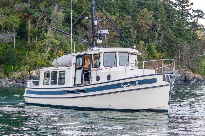 Slide: The Image of Nordic Tug 32 boat from 2000, cruising near a forested shoreline. - 14