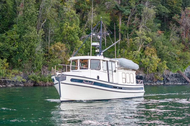 Slide: The Image of Nordic Tug 32 (2000) cruising on a serene lake with lush forest backdrop. - 12