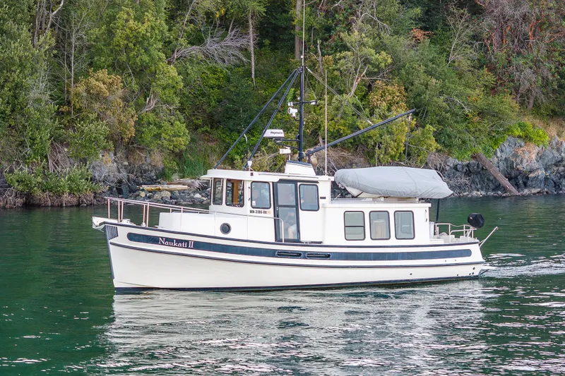 Slide: The Image of 2000 Nordic Tug 32 cruising on calm waters near a lush, forested shoreline. - 11