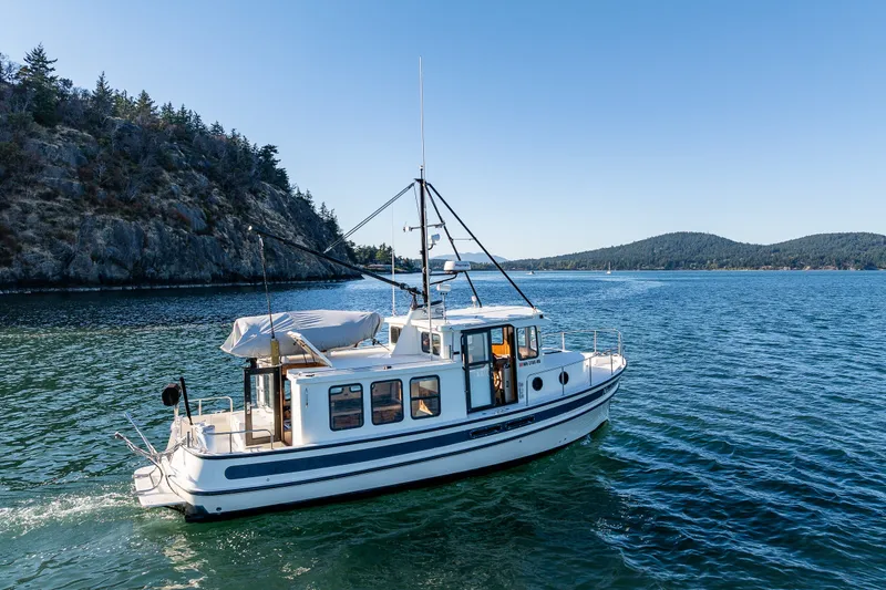 The Image of 2000 Nordic Tug 32 cruising on scenic waterway with rocky shoreline and forested hills. - 1