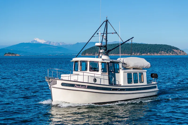 Slide: The Image of Nordic Tug 32 (2000) cruising on blue waters with scenic mountain backdrop. - 6