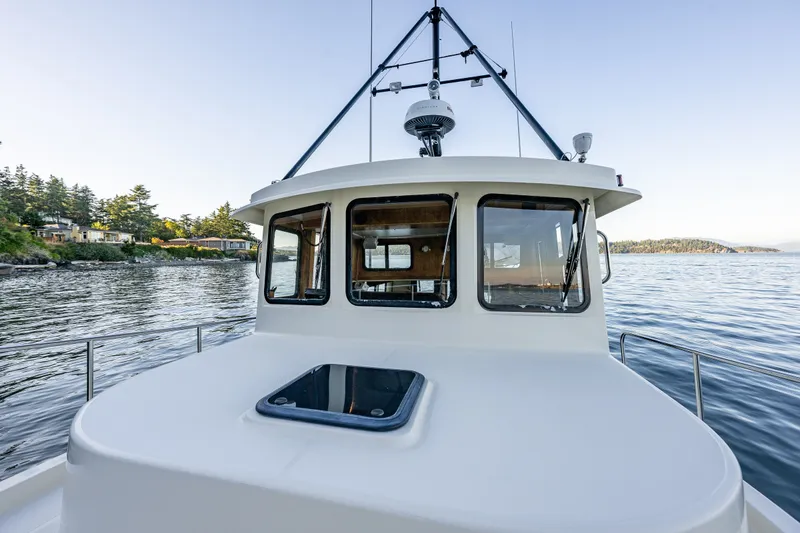 Slide: The Image of Nordic Tug 32 (2000) cruising on serene waters near a lush, tree-lined shore. - 28