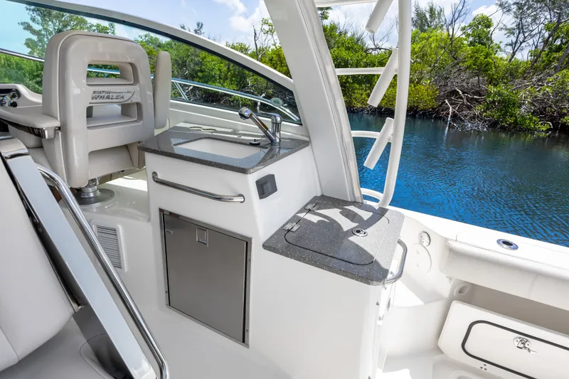 Slide: The Image of 2018 Boston Whaler 345 Conquest cockpit with sink and seating, near water and greenery. - 30