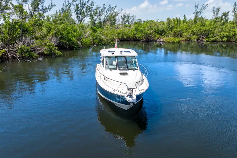 Slide: The Image of 2018 Boston Whaler 345 Conquest boat on calm water surrounded by lush greenery. - 10