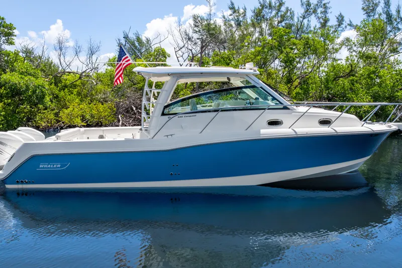 Slide: The Image of A blue and white 2018 Boston Whaler 345 Conquest sits calmly on the water, surrounded by trees. - 5