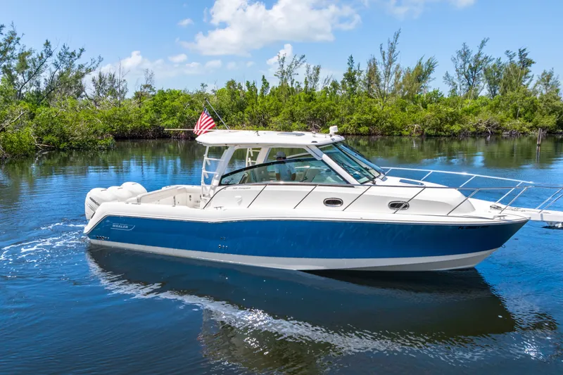 Slide: The Image of 2018 Boston Whaler 345 Conquest boat cruising on a serene waterway with lush greenery. - 1