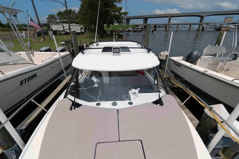 Slide: The Image of 2024 Jeanneau NC 795 Series 2 docked between boats, with bridge and trees in background. - 7