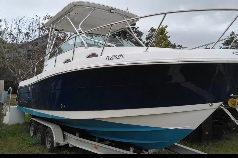 The Image of 2012 Robalo R305 Walkaround boat on trailer, blue and white hull, parked outdoors. - 0