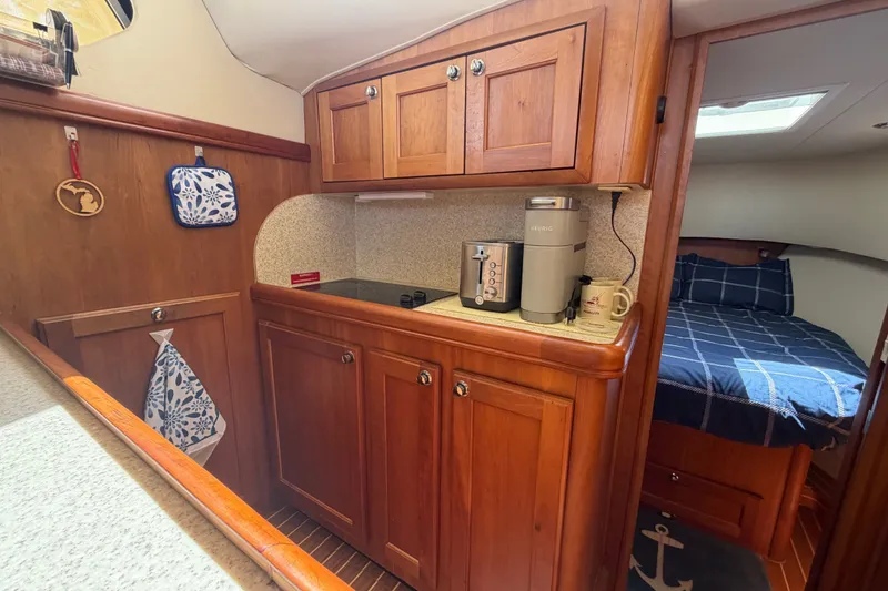 Slide: The Image of 2006 Mainship 34 Trawler interior with wooden cabinets, kitchenette, and cozy sleeping area. - 85
