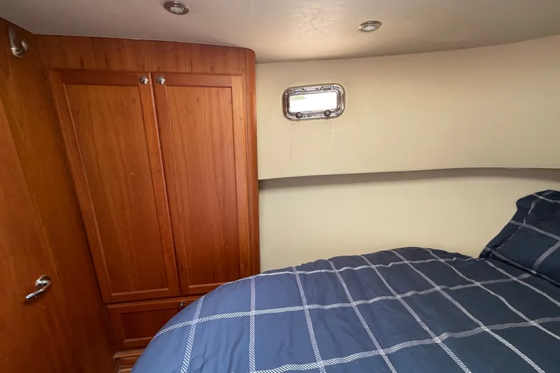 Slide: The Image of 2006 Mainship 34 Trawler cabin with wooden closet and bed, featuring a small window. - 90