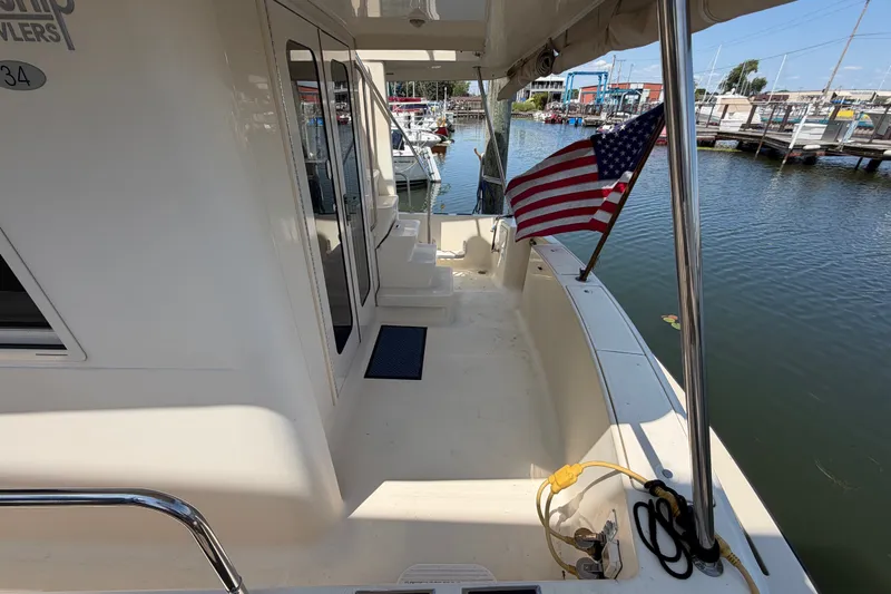 Slide: The Image of 2006 Mainship 34 Trawler docked, featuring American flag and spacious deck area. - 8