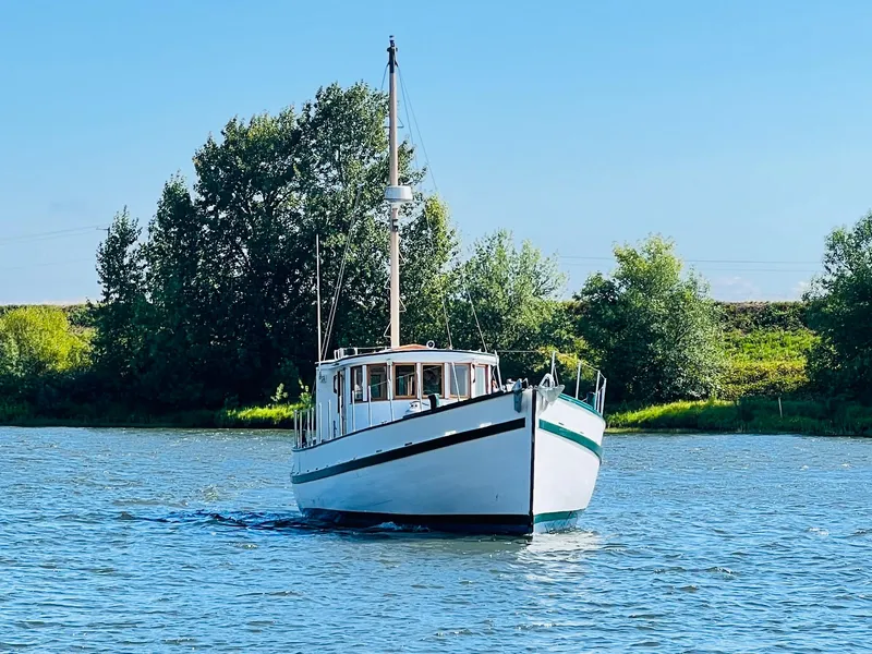 Slide: The Image of 1955 Colin Archer 42 boat cruising on a serene river with lush green trees in the background. - 45