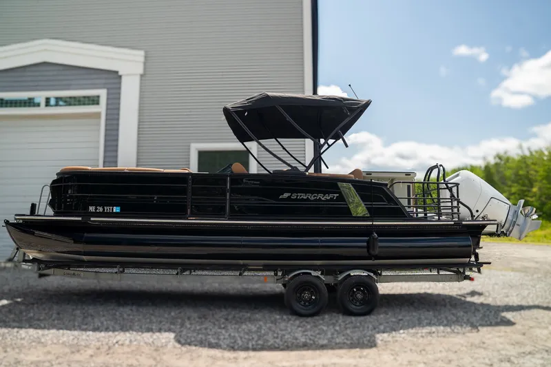 The Image of A 2025 Starcraft RX 25 DL BAR pontoon boat on a trailer in front of a building. - 1
