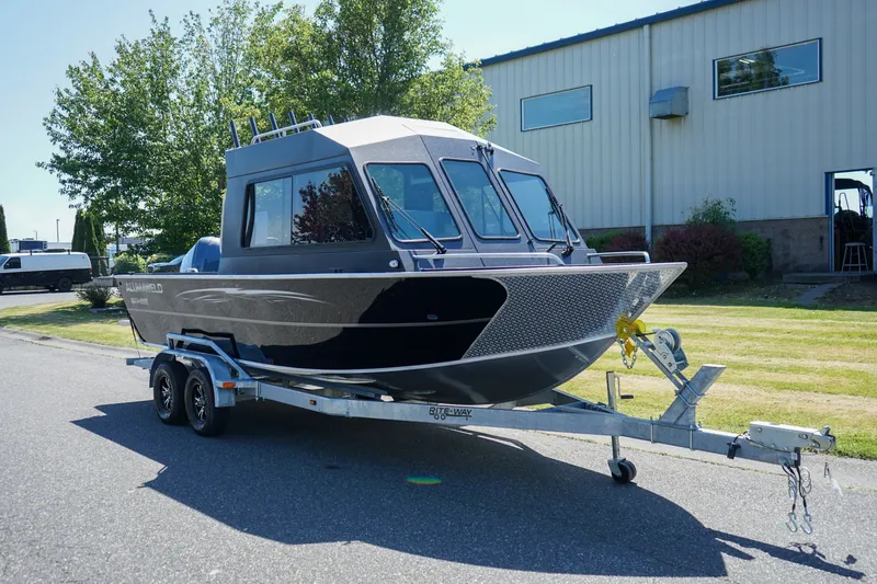Slide: The Image of 2026 Alumaweld Intruder Outboard 22 boat on trailer, parked outdoors near industrial building. - 2