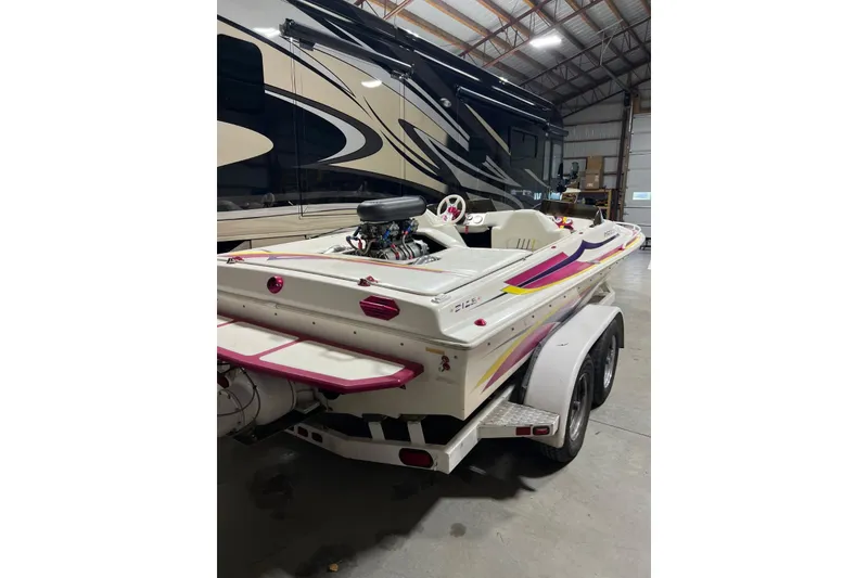 Slide: The Image of 1999 Shockwave 21LS speedboat with vibrant graphics, parked indoors on a trailer. - 12