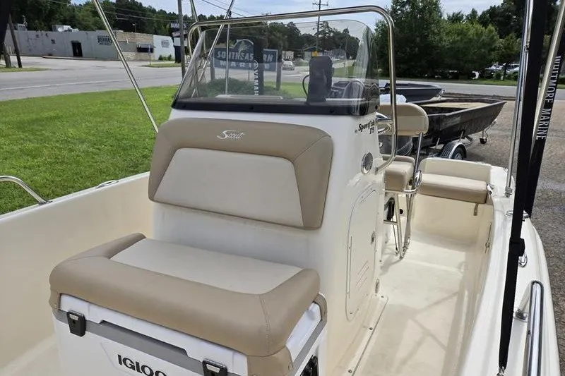 Slide: The Image of 2025 Scout 175 Sportfish boat interior with beige seating and console, parked outdoors. - 11
