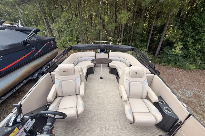 Slide: The Image of 2023 Crest Carribbean 250 SLC pontoon boat interior with plush seating and table, surrounded by trees. - 8