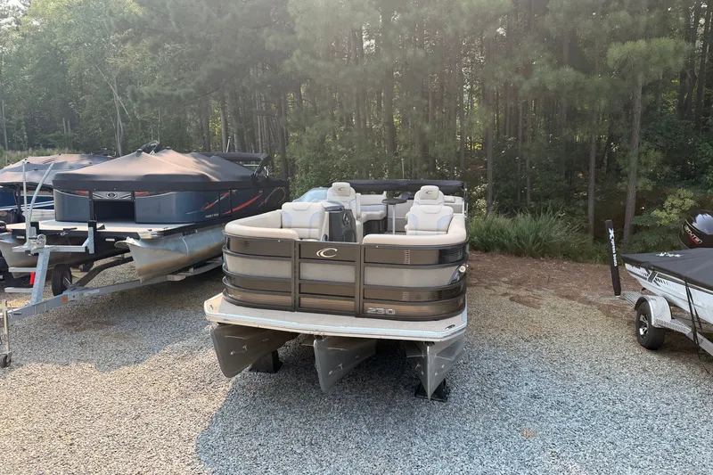Slide: The Image of 2023 Crest Carribbean 250 SLC pontoon boat parked on gravel near forest. - 2