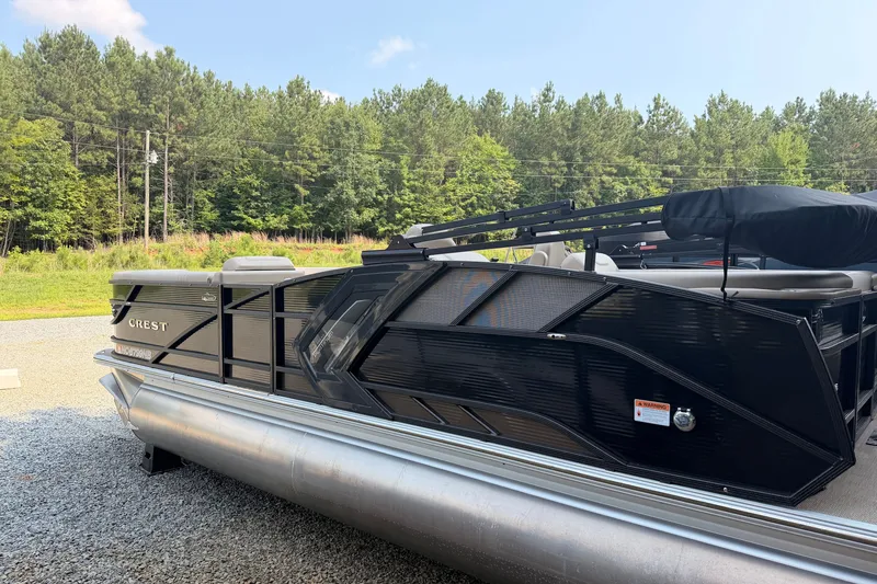 Slide: The Image of 2023 Crest Carribbean 250 SLC pontoon boat parked on gravel with forest background. - 1